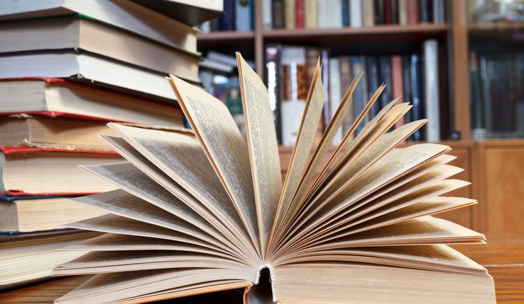 Zu sehen ist ein aufgeschlagenes Buch in einer Bibliothek, Foto: Colourbox